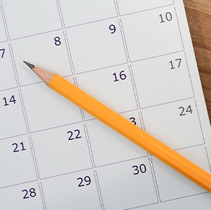 Paper calendar with pencil laid across it on a desk