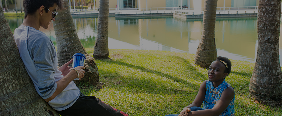 A female and male student sitting outside by a lake